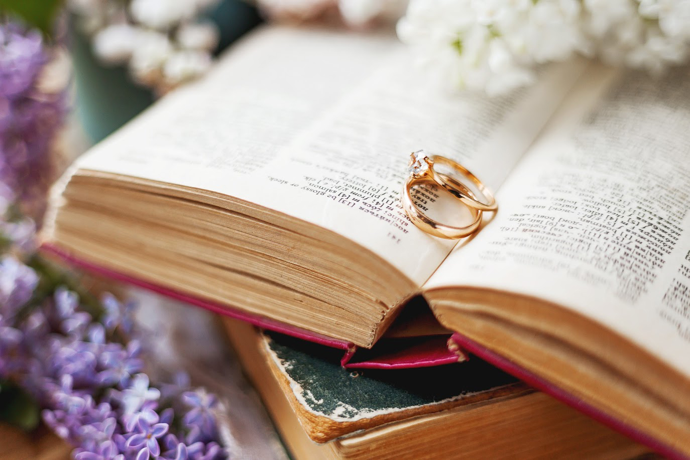 Pair of wedding rings with diamond. Rustic background with old books and lilac flowers. Retro background.